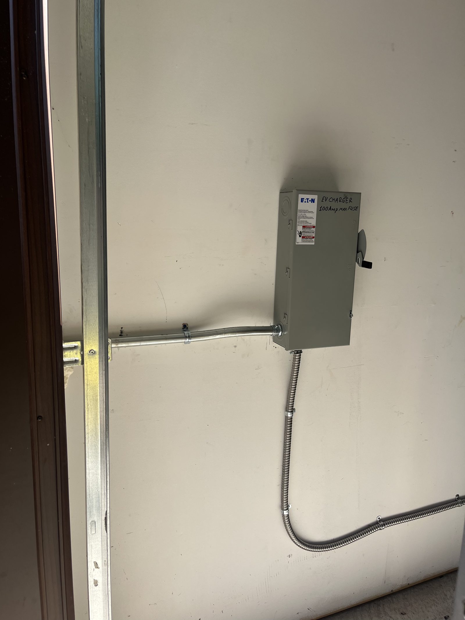 EV charger disconnect switch and conduit wiring installed in garage, labeled 100 Amp Max Fuse